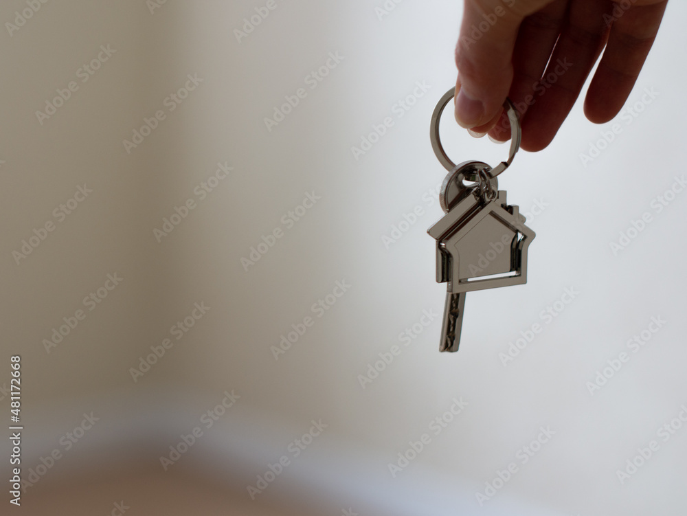Mortgage concept. Women hand holding key with house shaped keychain. Modern light lobby interior. Real estate, moving home or renting property. Mortgage concept. Women hand holding key with house shaped keychain. Modern light lobby interior. Real estate, moving home or renting property.