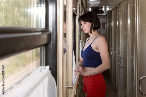 A smiling brunette woman in shorts and a tank top in the corridor of a moving train.