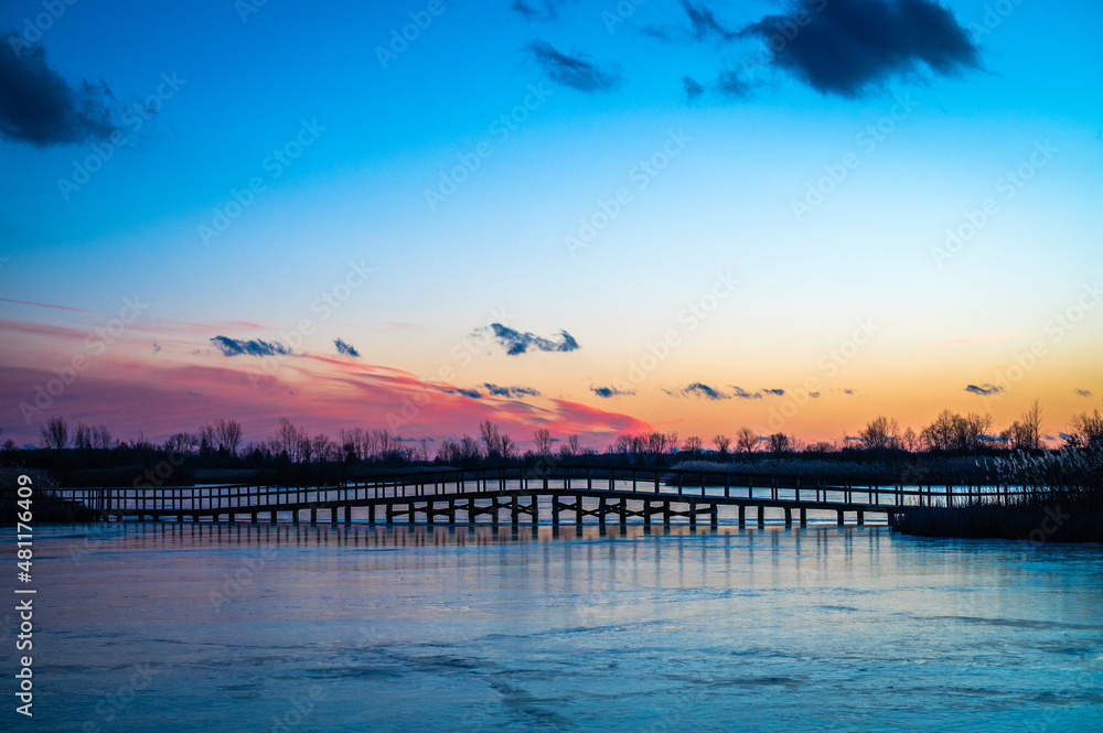Calming panorama view of a colorful sunset on a frozen lake over a bridge.