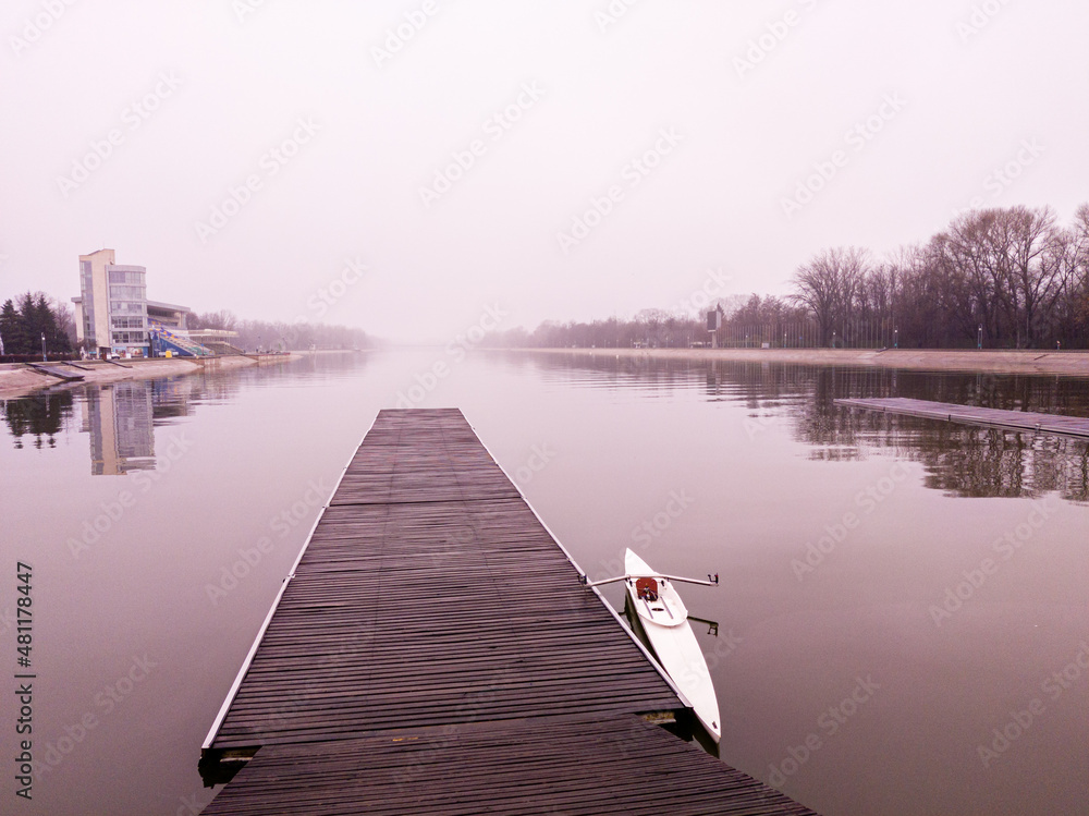Naklejka premium View to a lake, pier, boat and misty sky
