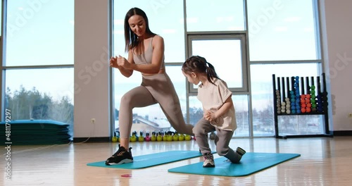 Attractive mom and daughter lunges together in the group practice room. Sports mom with daughter. High Quality.