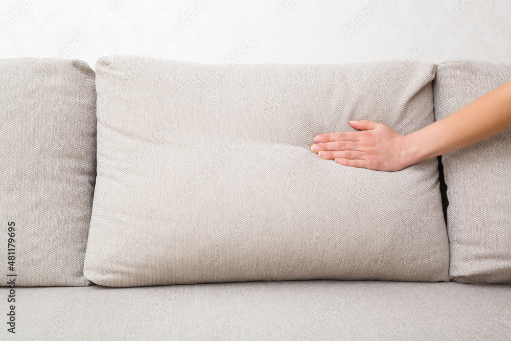 Young adult woman hand pressing light beige sofa back pillow for  comfortable sitting. Checking hardness and softness. Choice of the best  type and quality. Closeup. Stock Photo