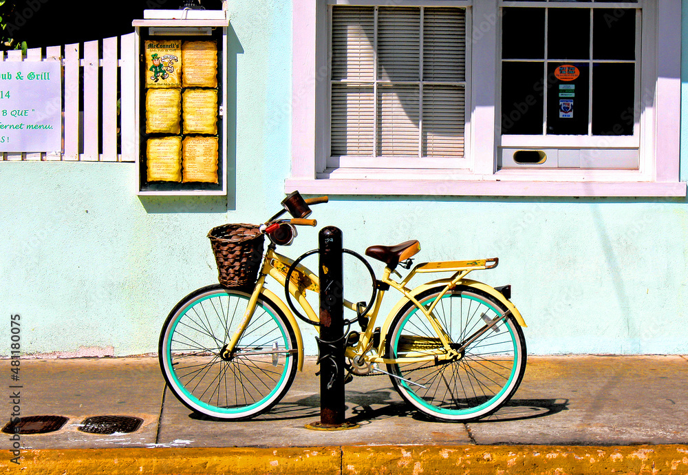 Bright yellow bicycle parked on a sidewalk,  leans against a post near a colorful building