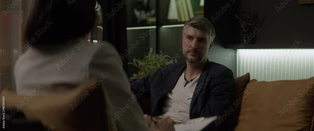 DOLLY IN Over the shoulder portrait of 40s Caucasian male having an appointment with his psychologist in the evening. Shot with 2x anamorphic lens DOLLY IN Over the shoulder portrait of 40s Caucasian male having an appointment with his psychologist in the evening. Shot with 2x anamorphic lens