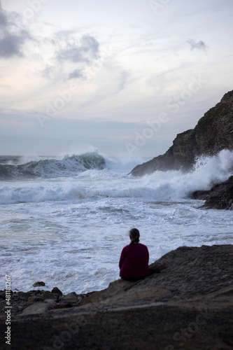 A woman watches waves coming in from Atlantic swells at Chapel Porth, Cornwall
