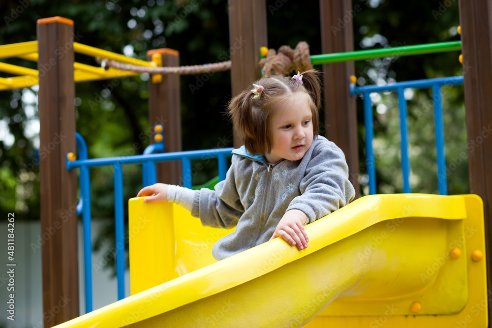 Cute child girl with ponytails plays on the playground - runs, climbs, rides on a swing and a slide. Outdoor active leisure Cute child girl with ponytails plays on the playground - runs, climbs, rides on a swing and a slide. Outdoor active leisure