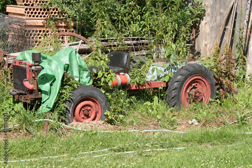 The abandoned wreck of a homemade tractor standing in the garden, overgrown with plants.  photo