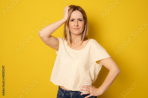 Young pensive woman in casual t-shirt standing isolated over yellow background.
