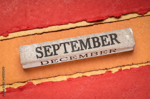 September text on grunge wooden block against handmade rag paper in red and orange tones, calendar concept
