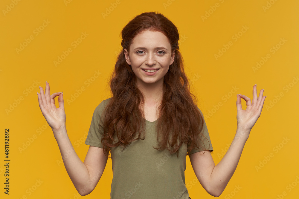 Indoor portrait of young ginger female keep calm and shows mudra gesture. isolated over yellow background Indoor portrait of young ginger female keep calm and shows mudra gesture. isolated over yellow background