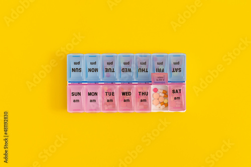 Daily pill box with medical pills on yellow background.