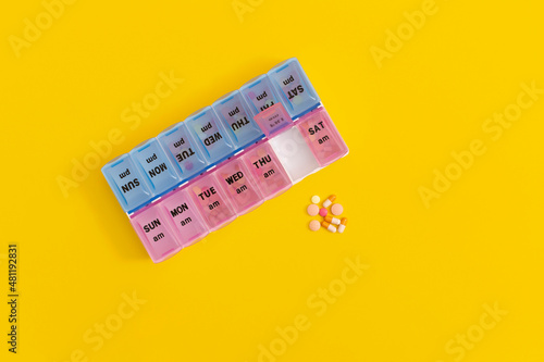 Daily pill box with medical pills on yellow background.