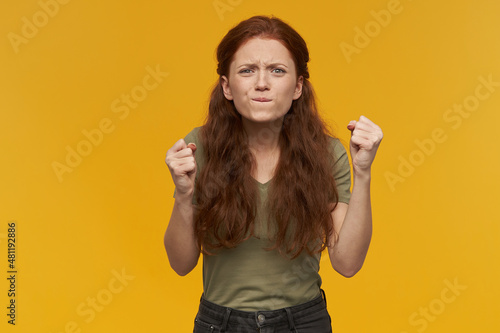 Indoor portrait of young ginger female bite her lip, raised hands while watching football game.. isolated over yellow background