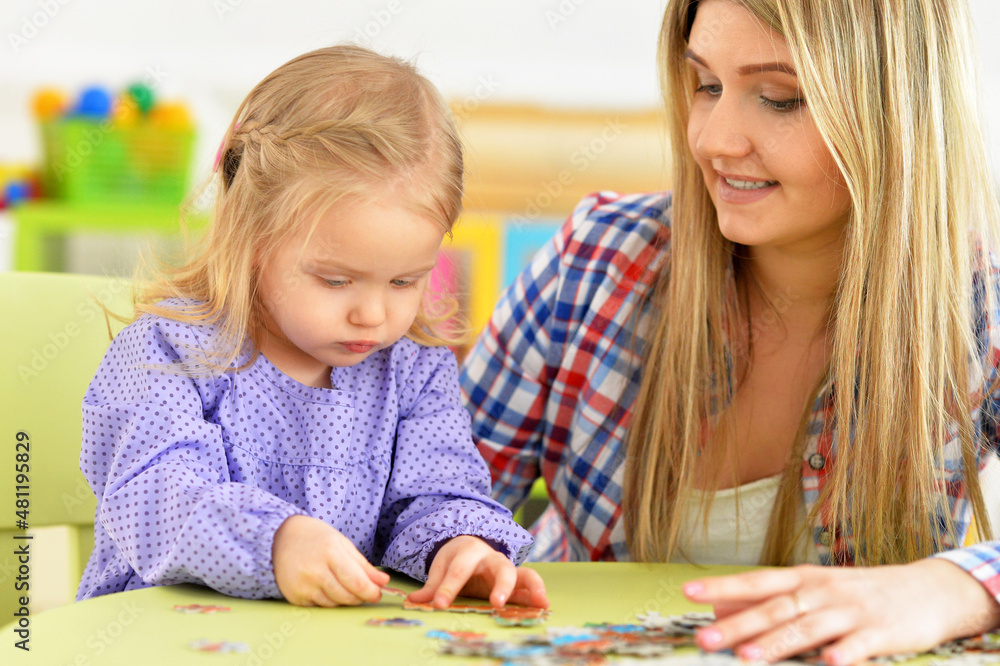 Portrait of mother with little daughter collecting puzzle