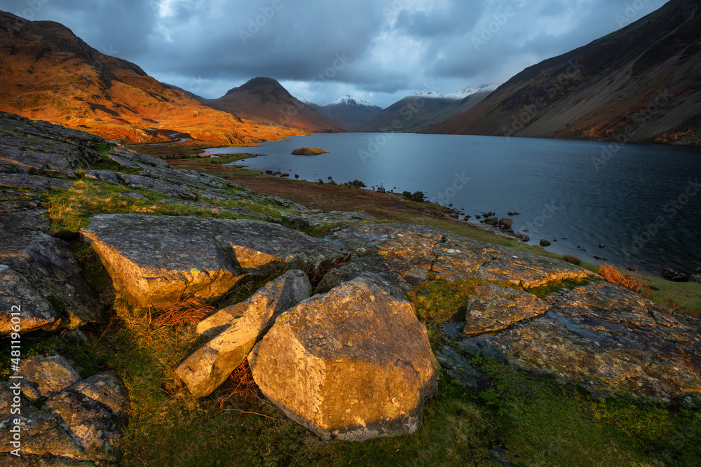 Dramatic view of Wastwater with dark clouds and golden light on landscape, Lake District, UK.