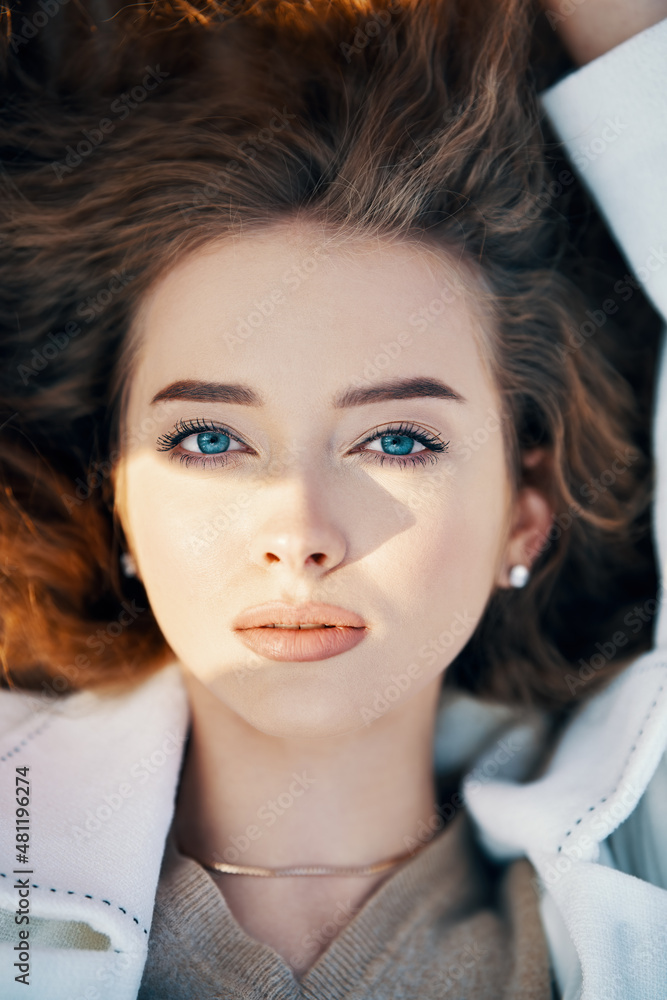 Naklejka premium Close-up portrait of pretty young woman with long wavy hair in sunlight outdoors