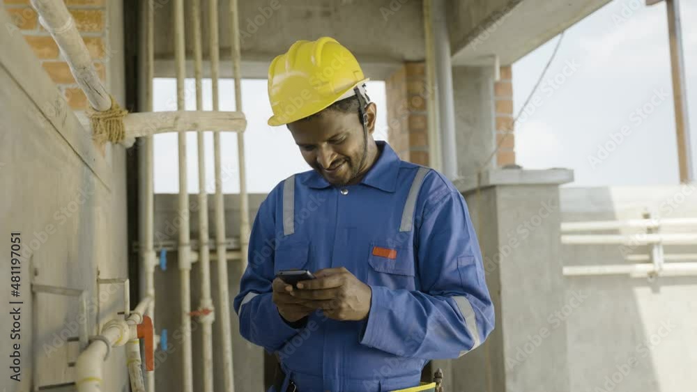 smilling young indian plumber or repairman busy by using mobile phone while working on industrial - concept of wasting of time by using social media, technology and internet distraction at workplace. smilling young indian plumber or repairman busy by using mobile phone while working on industrial - concept of wasting of time by using social media, technology and internet distraction at workplace.