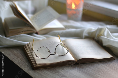 Open books, reading glasses and lit candle on the table. Selective focus.