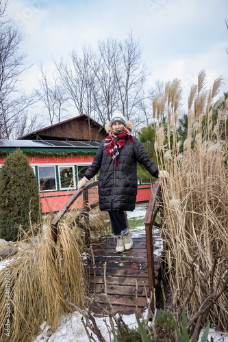 a girl in a raincoat and a checkered scarf stands on a decorative wooden bridge in winter  photo