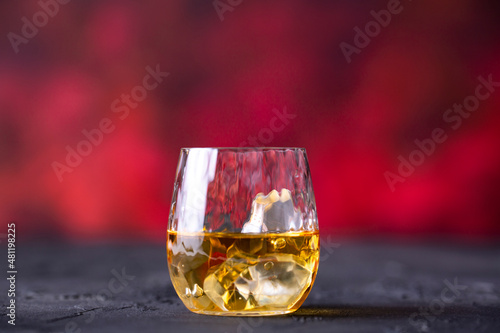 Glass of whiskey with ice placed in front of red background
