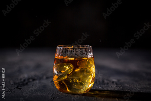 Glass of whiskey with ice placed in front of black background