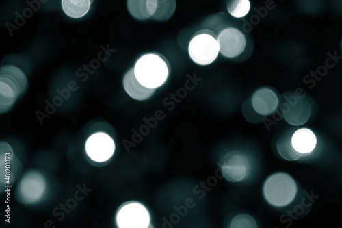Tidewater Green colors. Defocused bokeh christmas white lights on dark green background. Blurred abstract green glitter texture. Green bokeh glitter wallpaper for Christmas, New year.