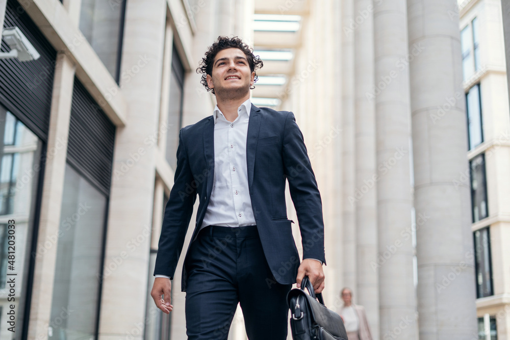 A confident, satisfied male manager in an official suit goes to the office and holds a briefcase with documents and coffee in his hands A confident, satisfied male manager in an official suit goes to the office and holds a briefcase with documents and coffee in his hands