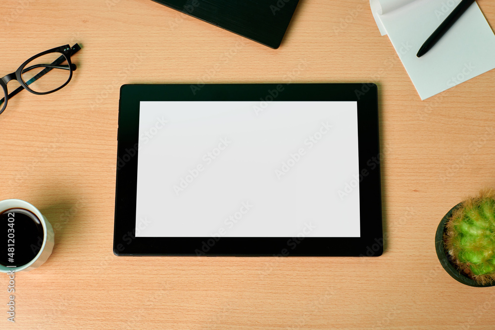 Top view of a tablet with a group of business objects on a wooden desk. Flat lay, mock up