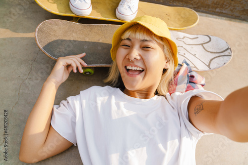 Asian girl laughing and taking selfie photo while lying on skateboard