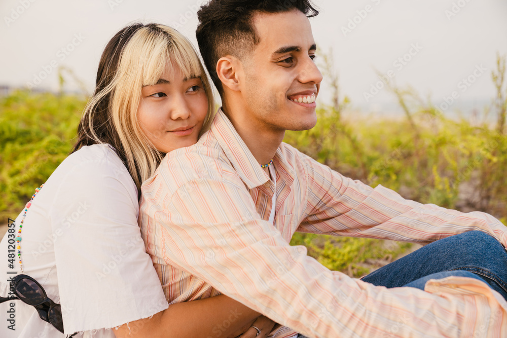 Multiracial couple smiling and hugging while resting on beach Multiracial couple smiling and hugging while resting on beach