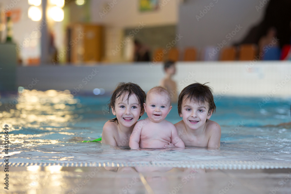 Three little children,  cute baby boy and two older brothers, swimming happily in a shallow pool