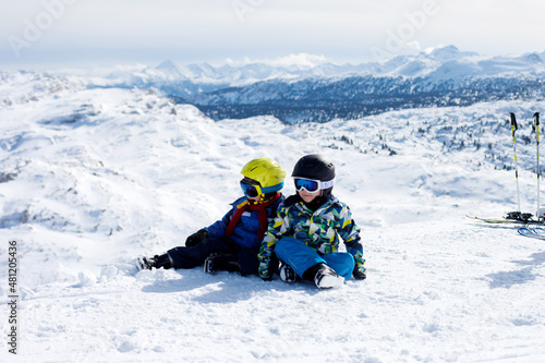 Two young children, siblings brothers, skiing in Austrian mountains on a sunny day