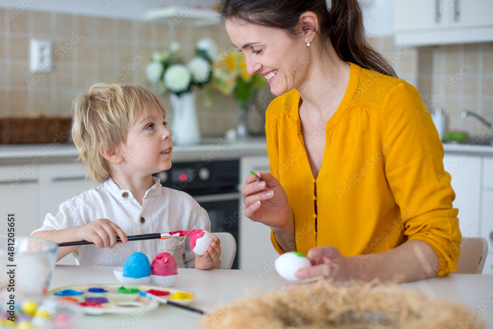 Fototapeta premium Beautiful blond child, toddler boy, painting easter eggs with mother at home, making easter wreath
