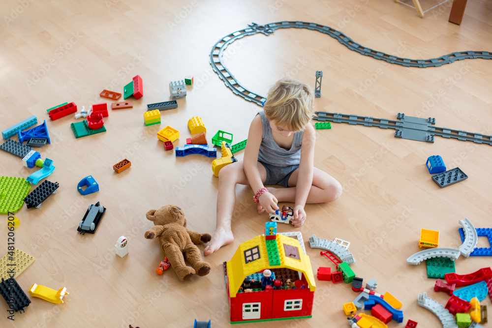 Foto Stock Cute child, playing with colorful toy blocks. Little boy  building house of block toys sitting on the floor in sunny spacious bedroom  | Adobe Stock
