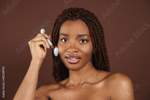 Half-naked black woman massaging face with jade roller photo