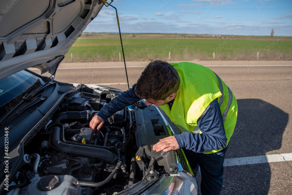 Young man looking under the hood of a broken down car Young man looking under the hood of a broken down car