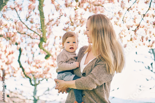 Outdoor portrait of happy young mother with adorable baby girl under blooming spring tree, bottom view © annanahabed