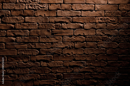 Brick wall with rough red masonry. Abstract background with illumination from lantern.