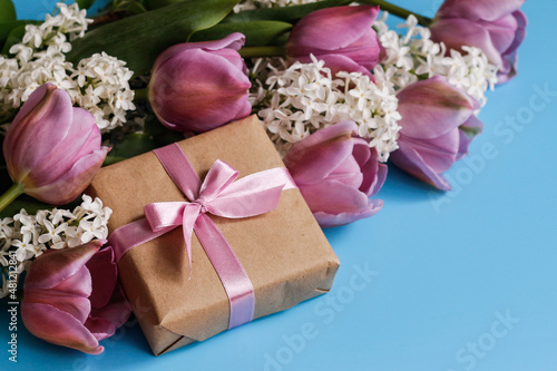 Spring bouquet of tulips and lilacs and gift box on blue background
