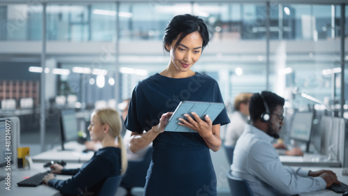 Successful Businesswoman in Stylish Dress Using Tablet Computer, Standing in Modern Diverse Office Working on Financial, Business and Marketing Projects. Portrait of Beautiful Asian Manager. photo