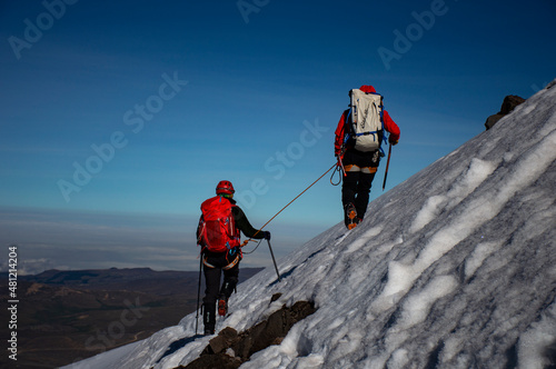Fotografie, Tablou Mountain guide taking care of her client on a snow covered slope in Chimborazo volcano