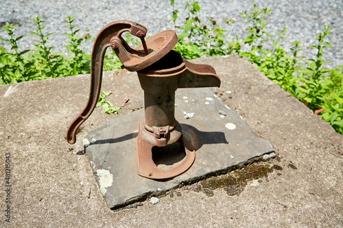 Rusty Manual Water Pump on Stone Well Cap with Moss