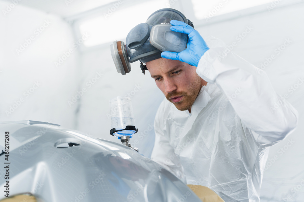 Young male car painter checks the quality of painting. Car service worker at work Young male car painter checks the quality of painting. Car service worker at work