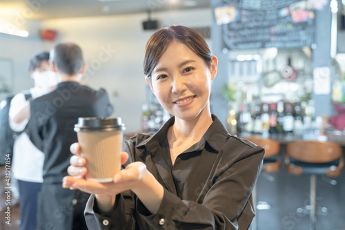 テイクアウトのコーヒーを渡す女性カフェ店員