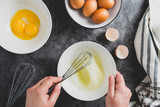 Cooking omlette. Woman's hands cookingomlette, breaking an fresh egg. Dark background. Food flat lay.