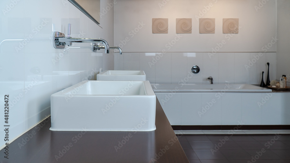 Modern bathroom in white and brown with two sinks, bathtub and wooden furniture. Selective focus on the front Modern bathroom in white and brown with two sinks, bathtub and wooden furniture. Selective focus on the front