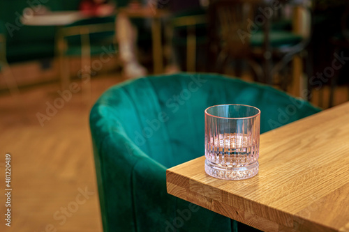A pink glass of water on the edge of a wooden table at the cafe, a green chair photo