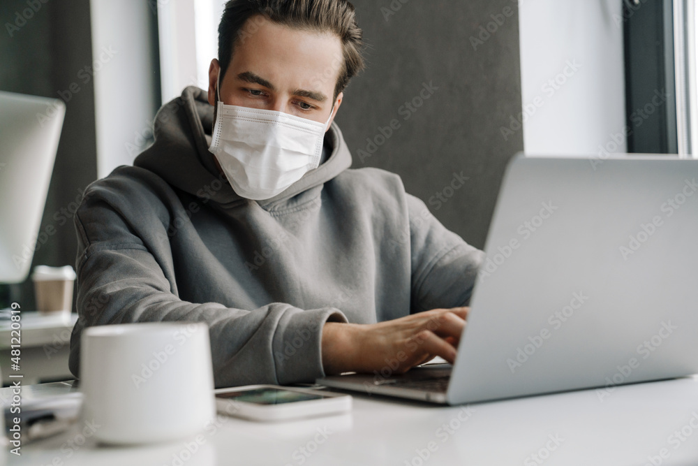 Young man in protective mask working with laptop at office Young man in protective mask working with laptop at office