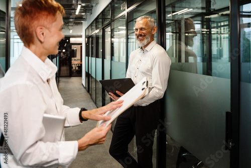 Mature white colleagues smiling while working in office