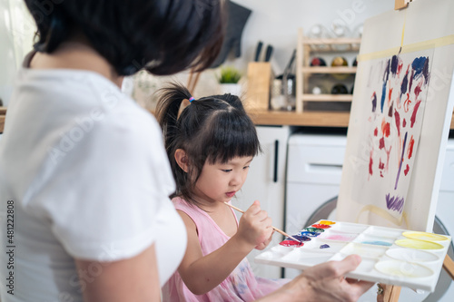 Asian young happy kid daughter coloring on painting board with mother. 